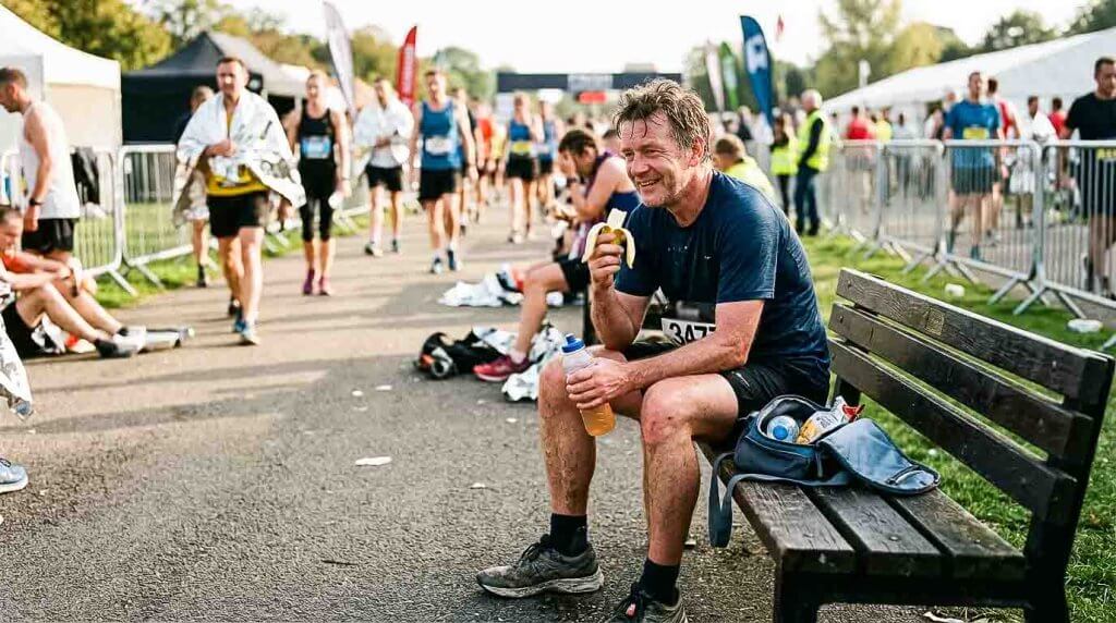 Essen und Trinken nach dem Marathon Läufer isst nach dem Marathon eine Banane und trinkt