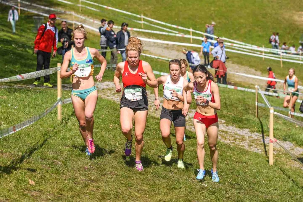Hügelläufe – Bergauflaufen beim Crosslauf Vier Läuferinnen beim Crosslauf auf einer ansteigenden Wiesenstrecke
