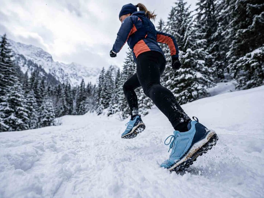 Laufen im Schnee – Lauftraining im Winter Läuferin beim Laufen im Schnee auf einem verschneiten Winterweg