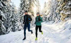 Läufer und Läuferin beim Laufen im Winter auf verschneitem Waldweg